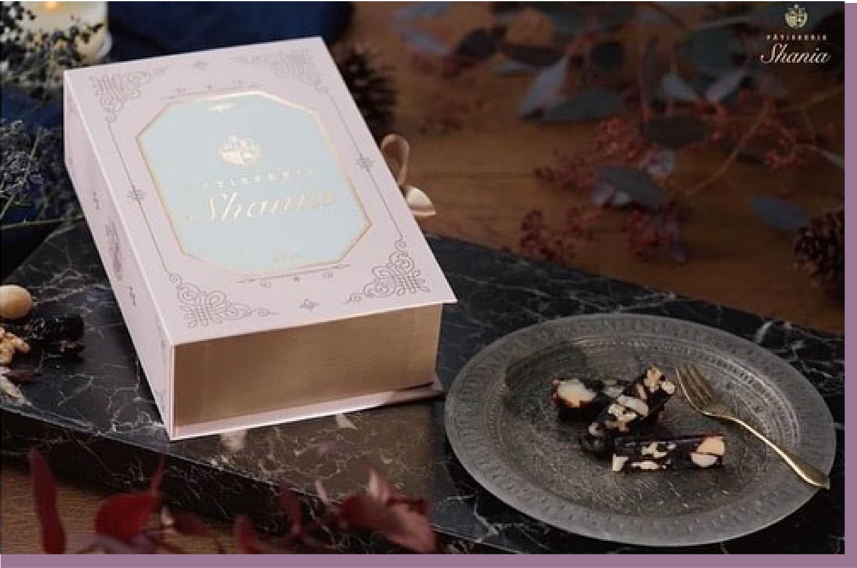 這是一個盒子放置在有著大理石紋路桌面上。禮品盒的顏色為柔和的粉色，上面印有金色的品牌名稱“Shania”和裝飾性圖案。