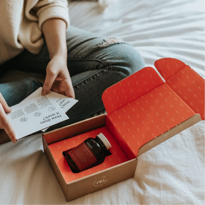 在床上擺放了一個紅色的郵寄盒，盒內放了一瓶健康食物，瓶上貼有紅色標籤。