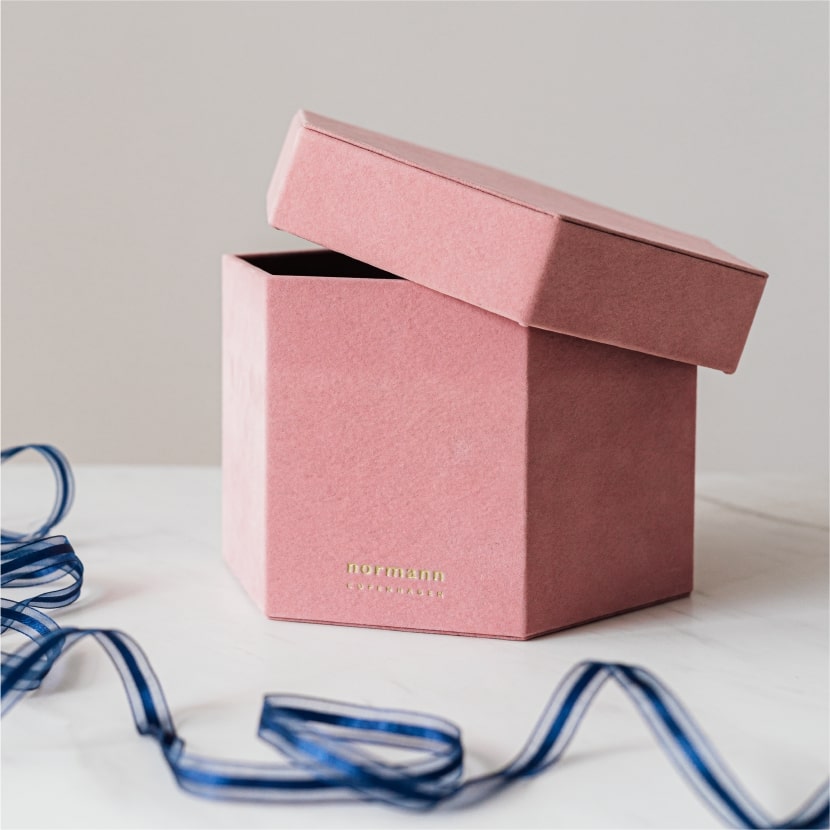 在白色的背景下，白色的枱上擺放了一個六角形的粉紅色天地蓋盒，枱前更放有一條藍色的包裝絲帶。