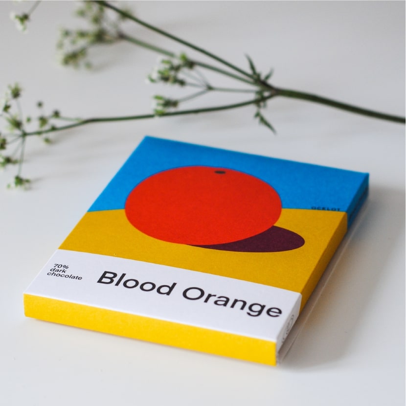 在白色的枱上擺放了一本橙色的書型硬盒，盒上印有"Blood Orange" 的字眼和橙的圖案。