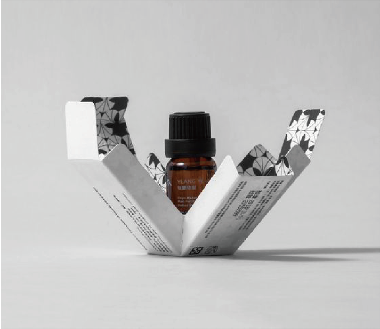 在白色的背景下，一個白色的包裝盒向四方打開，中間有一支黑色蓋，啡色的透明玻璃樽。