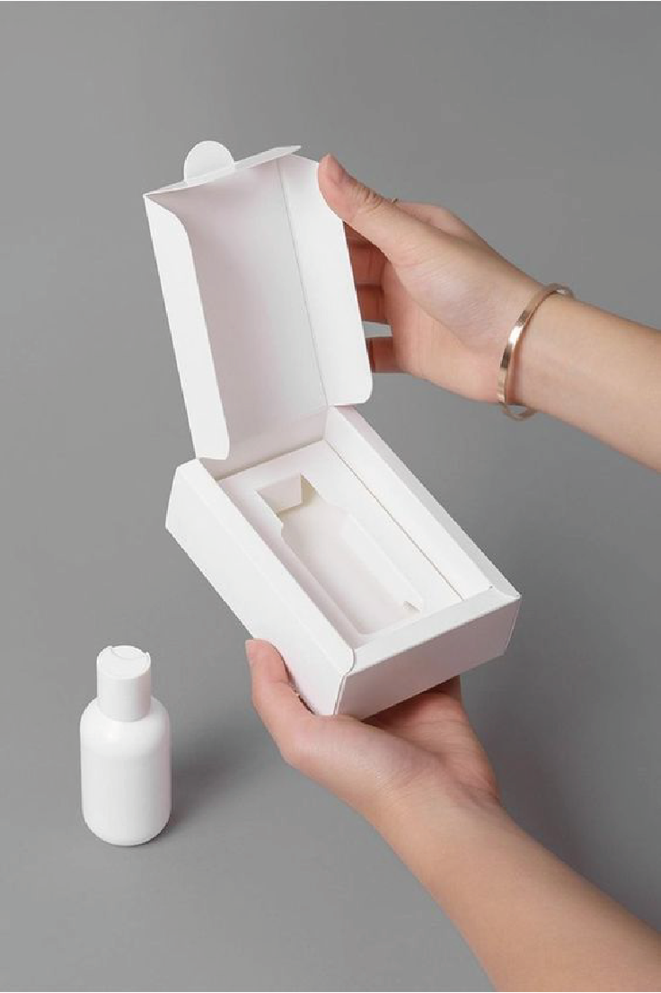 在灰色的背景下，一雙手打開了純白色的包裝盒，下面有一支純白色的樽。