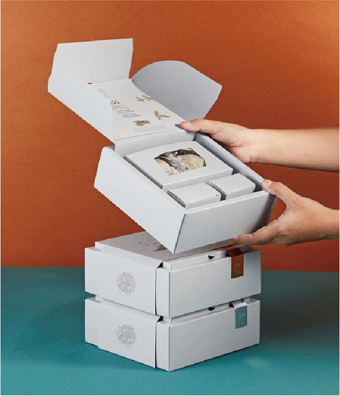 在橘色的背景下，有三個以堆疊方式擺放的郵寄盒，其中最上方的郵寄盒被打開，展示盒內的產品。