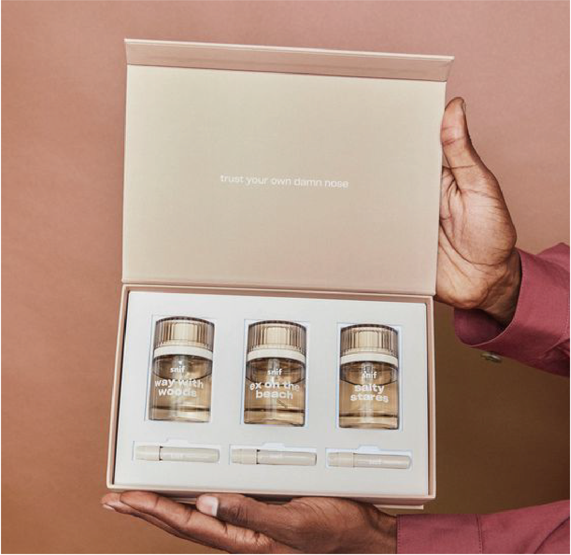 在啡色的背景下，一個打開的郵寄盒，盒內擺放了三枝化妝水。