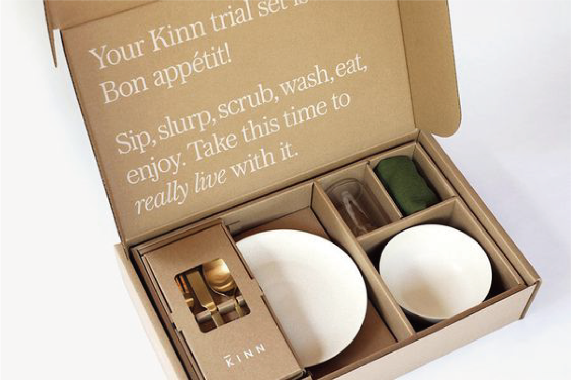 在白色的背景下，一個打開的郵寄盒，盒內擺放了餐具套裝，包括碟、碗和刀叉。