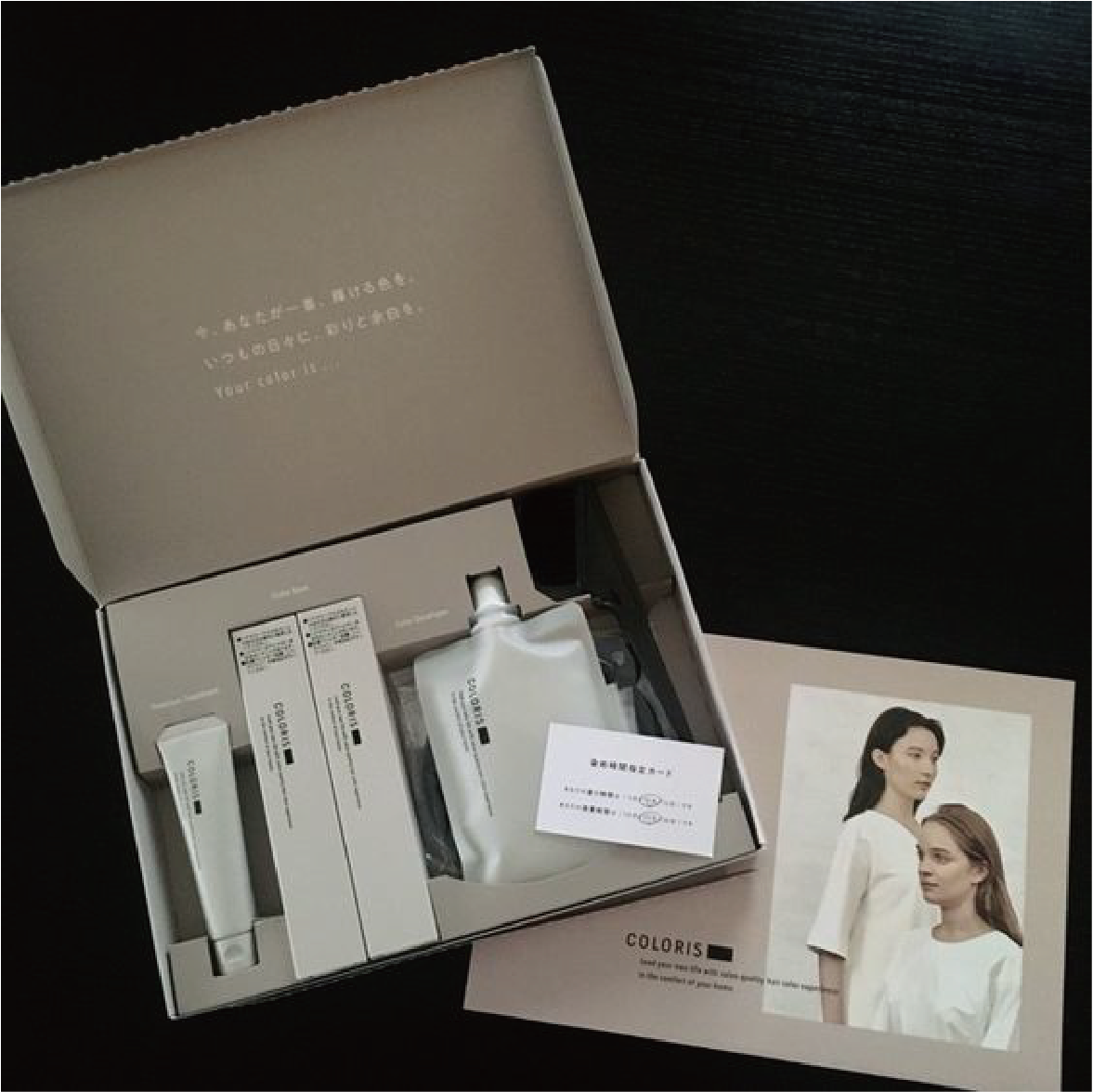 在黑色的背景下，一個打開的郵寄盒，盒內擺放著一套化妝用品套裝。