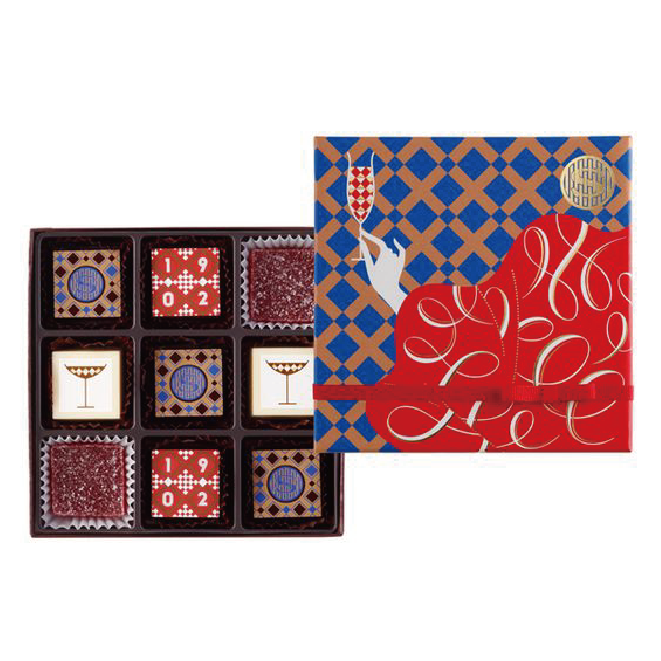 在白色的背景下，擺放了一盒朱古力禮盒，盒內以九格隔板分開朱古力，盒蓋則印帶以穿紅衣的女性高舉酒杯的抽象畫。