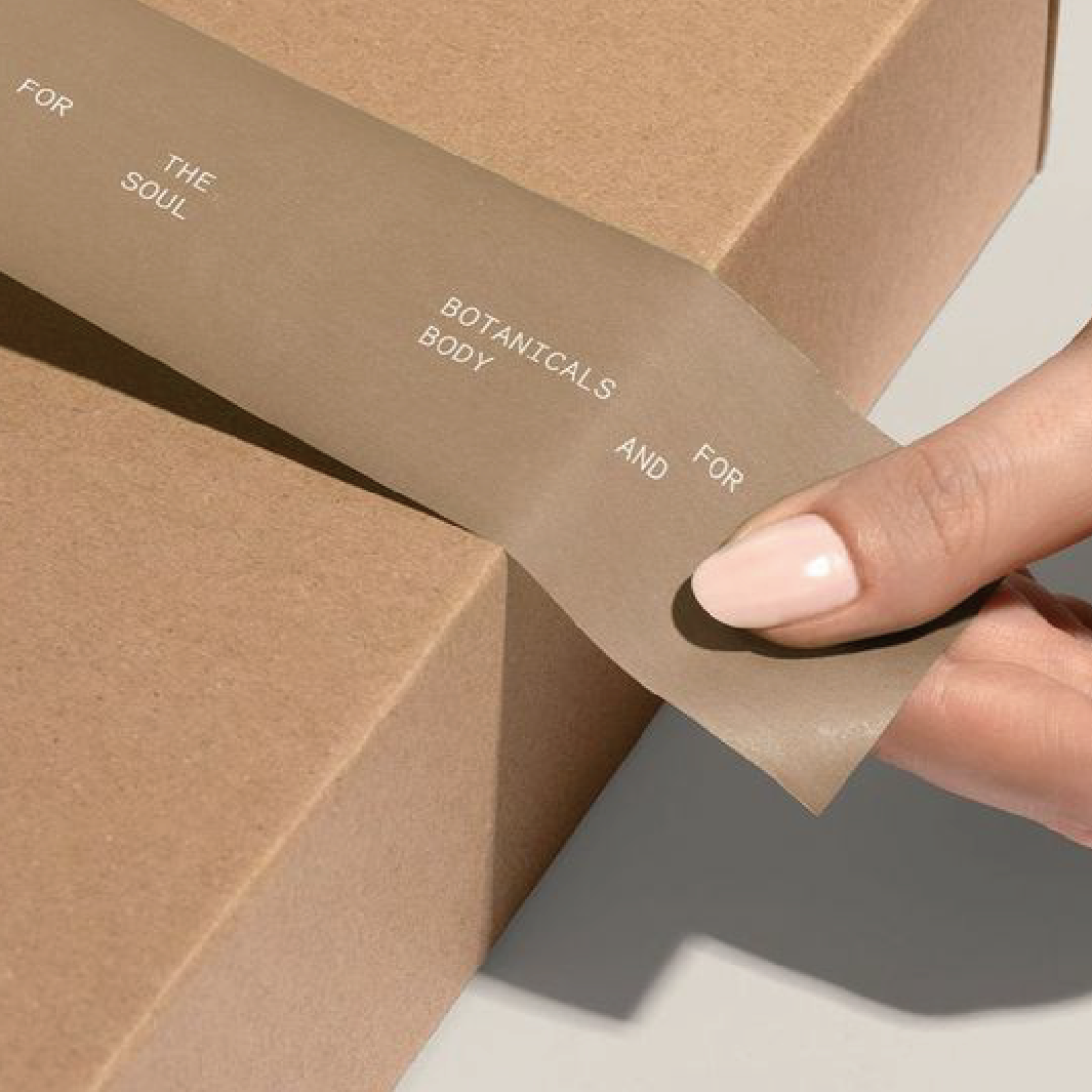 有一隻手為一個啡色的盒貼上包裝貼紙。