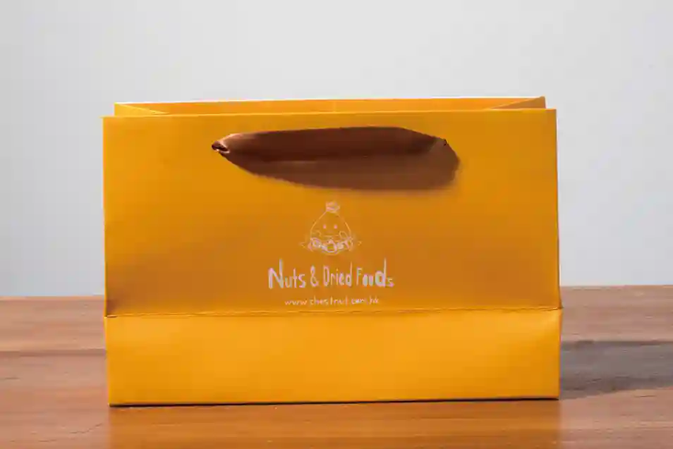 A mockup of a ribbon paper bag displayed on a gray background and wood grain tabletop