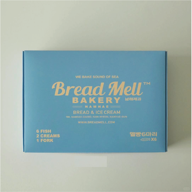 A minimalist bakery box in ocean blue. The front of the box is printed with 'Bread Mell Bakery' and 'We bake sound of sea' in gold lettering, and is labelled with a description of the bread and ice cream in English.
