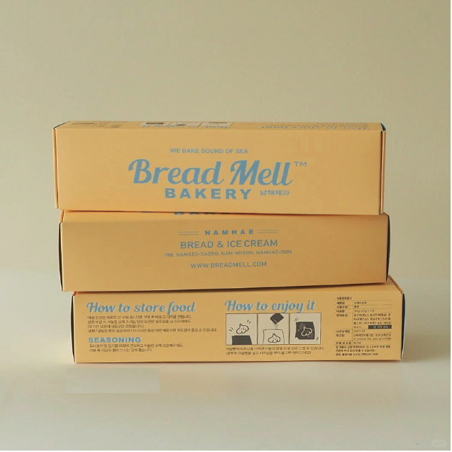 Three stacked gold coloured bakery boxes with the slogans 'Bread Mell Bakery' and 'We bake sound of sea' printed on the top box. The bottom box displays guidelines for enjoying the food, including illustrated serving instructions.