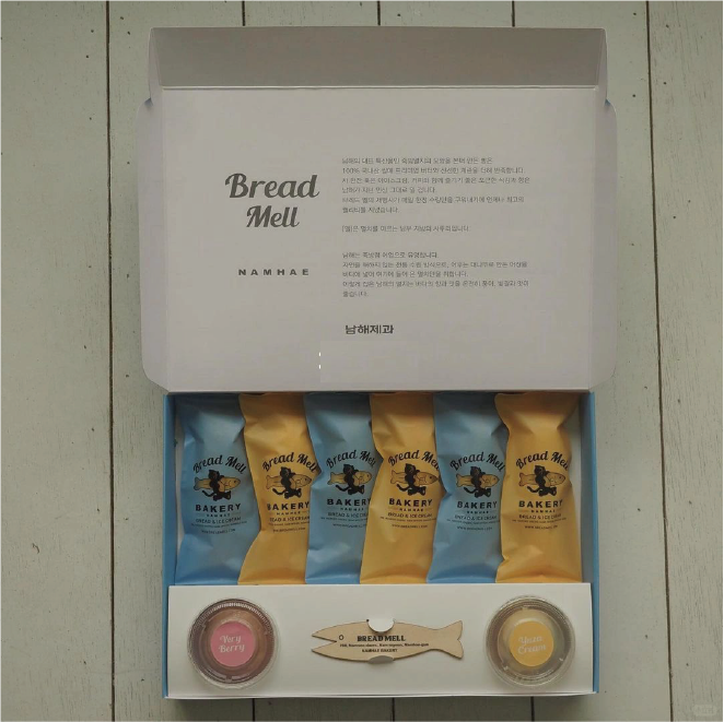 Open bakery box with neatly arranged golden and blue packages of baked goods and two small bottles of bread model decorations