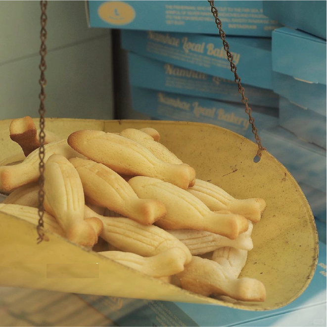 Freshly baked breadsticks hanging on a metal scale with stacked blue bakery boxes in the background
