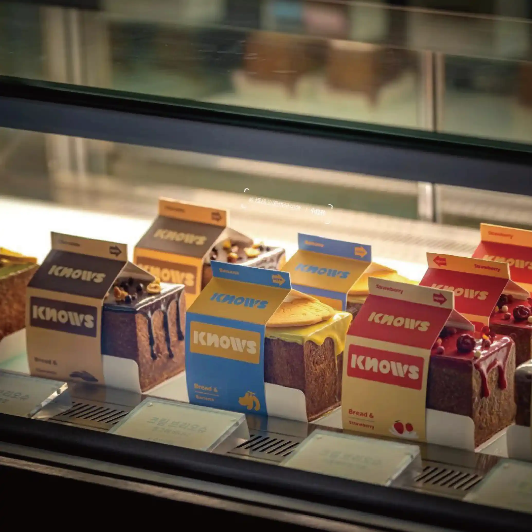 A number of cakes displayed in the freezer of the pastry shop, each with a different colour "KNOWS" branded box reflecting the various flavours.