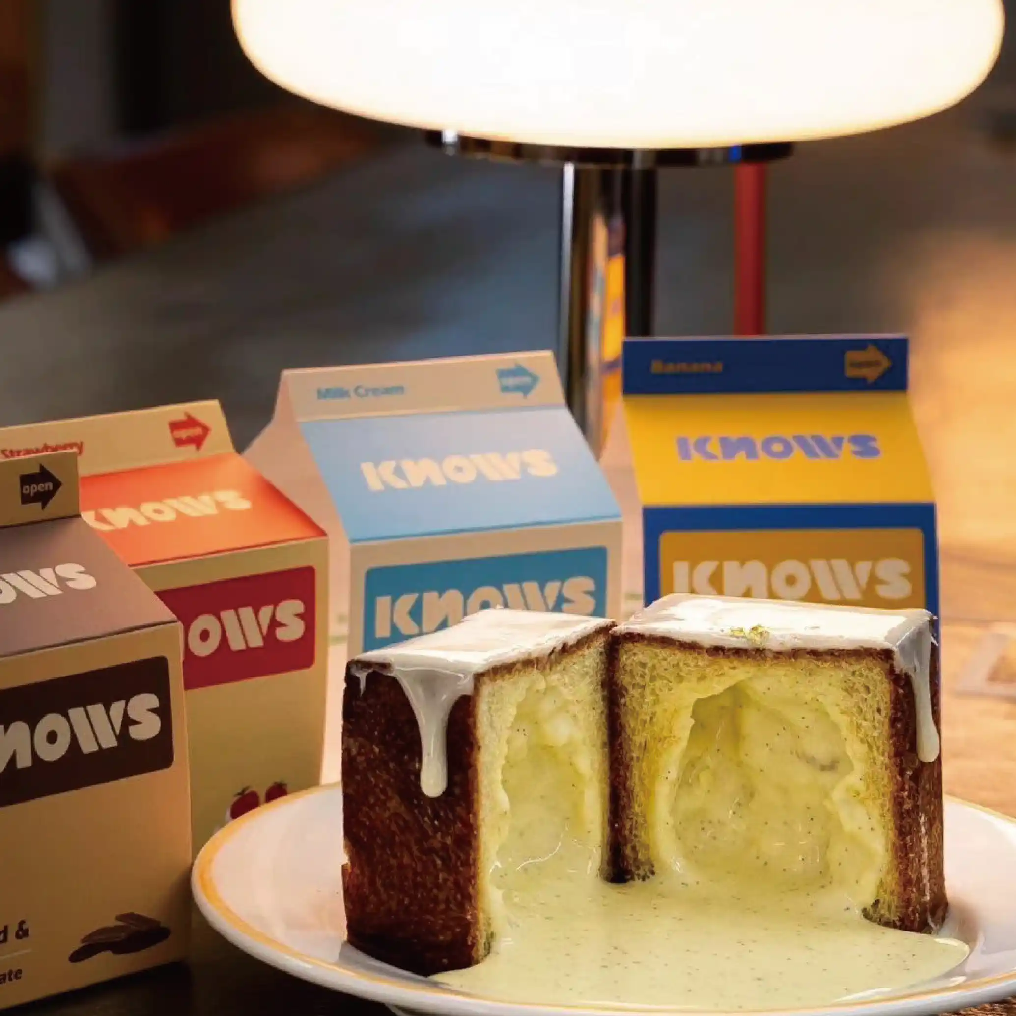 A half-sliced cake with a smooth buttercream layer in the middle, next to a yellow and blue "KNOWS" branded box.