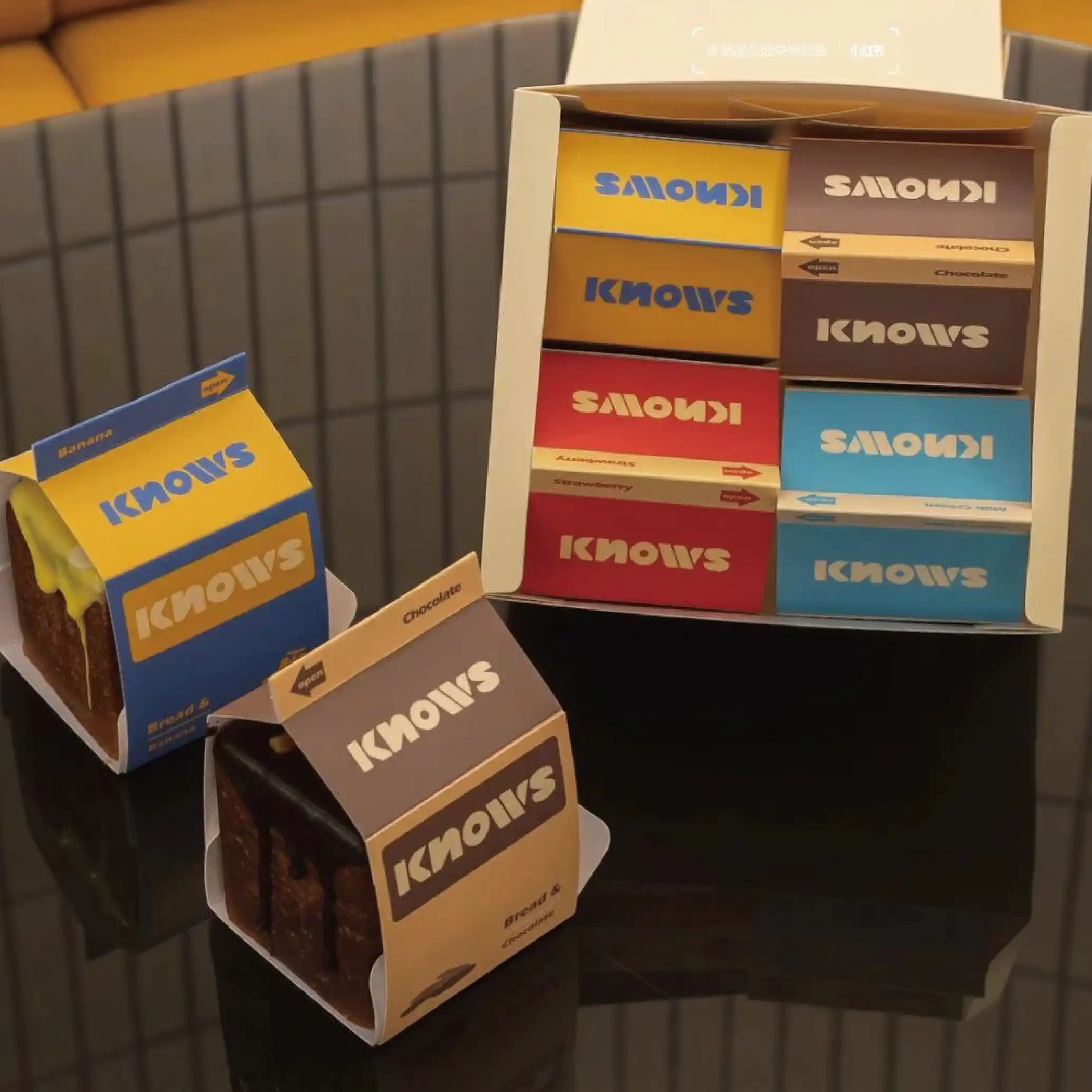 Multiple "KNOWS" branded cake boxes are stacked on top of each other, each with a different colour scheme to mark the different cake flavours.