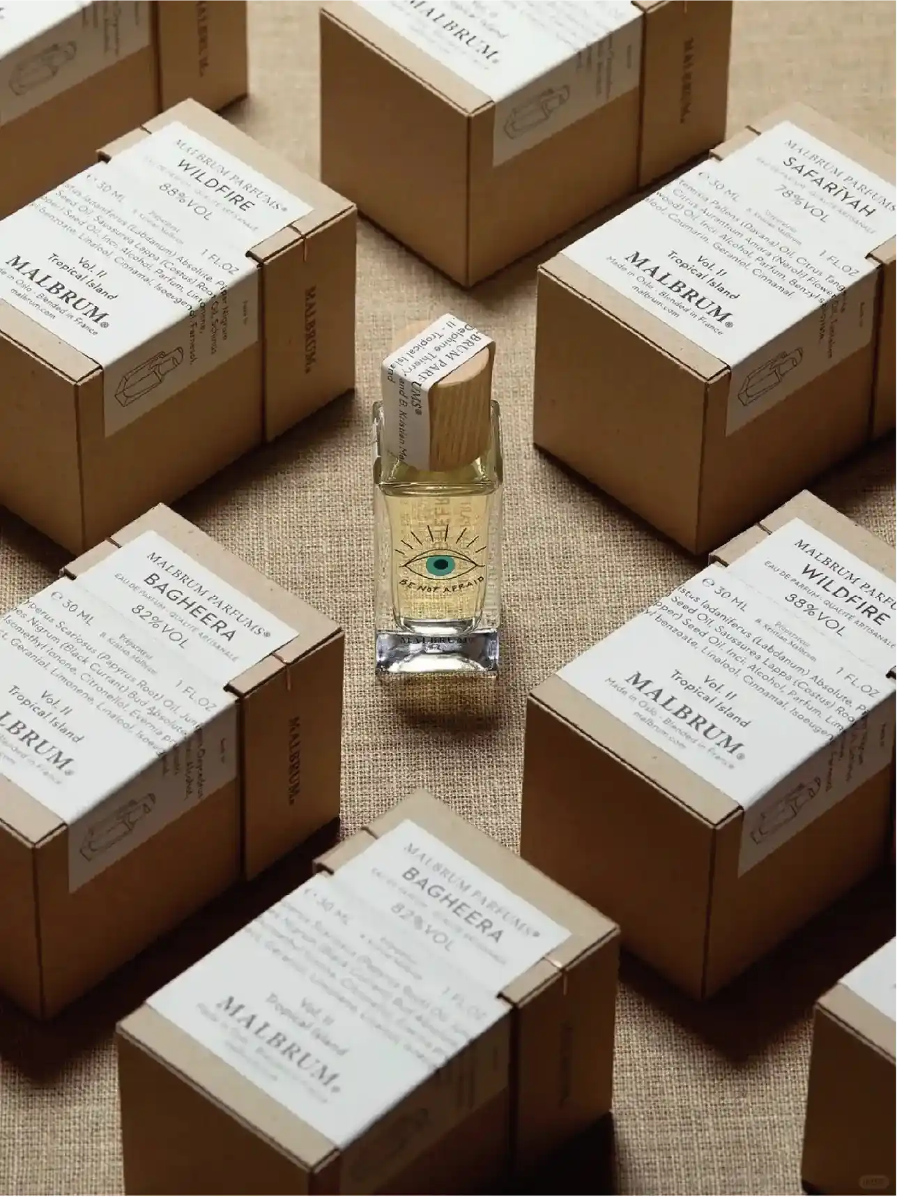 A transparent bottle of perfume sits between brown cardboard packaging that has the brand name and specific information about the perfume printed on it.