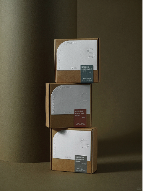 Three different types of soap boxes are stacked together with different coloured labels to introduce the features of each soap, such as 'MADDER CHAMOMILE' and 'RICE MILK EXFOLIATE'.