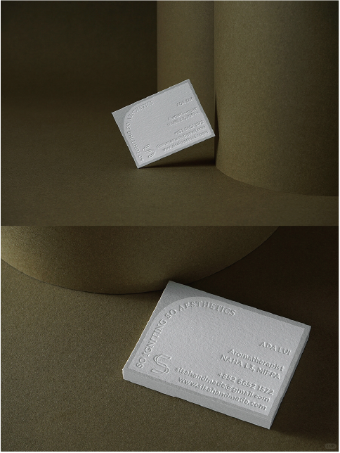 A business card lying on a brown background with raised white text 'SO GIFTING SO AESTHETICS' and 'MAKER' and contact information for the card holder.