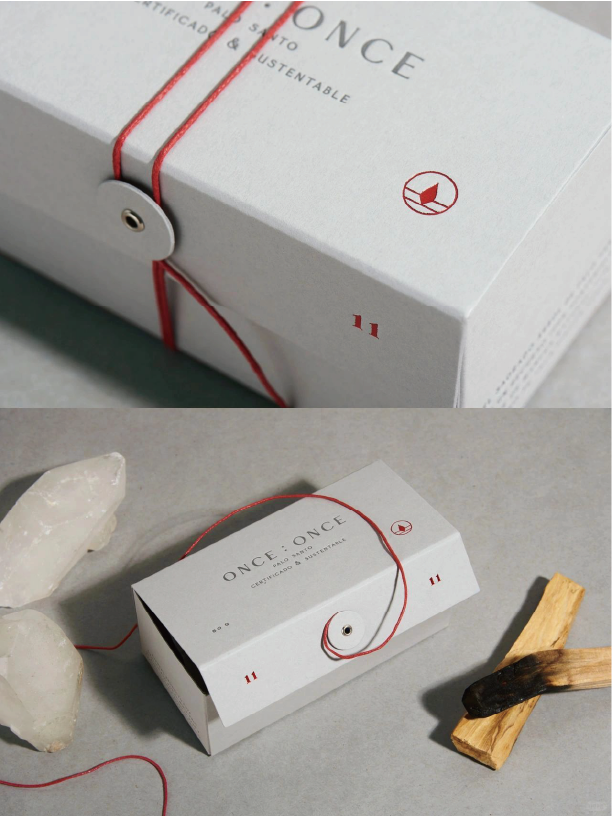 White box with "ONCE : ONCE" and the eco-logo, sealed with a red string, next to crystals and burnt wood.