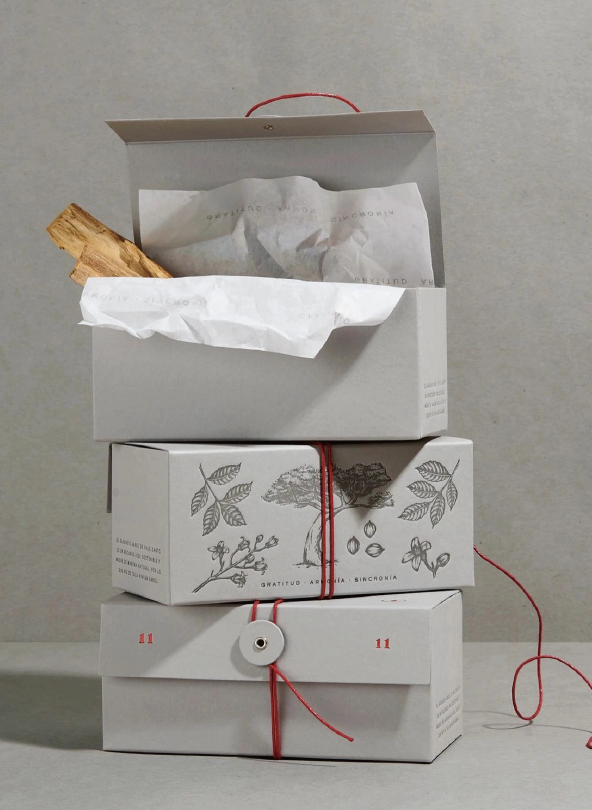 Stacked white box with top lid opening to reveal wrapping paper and wood. The box is printed with botanical illustrations and text, tied with red thread and embellished with a circular label.