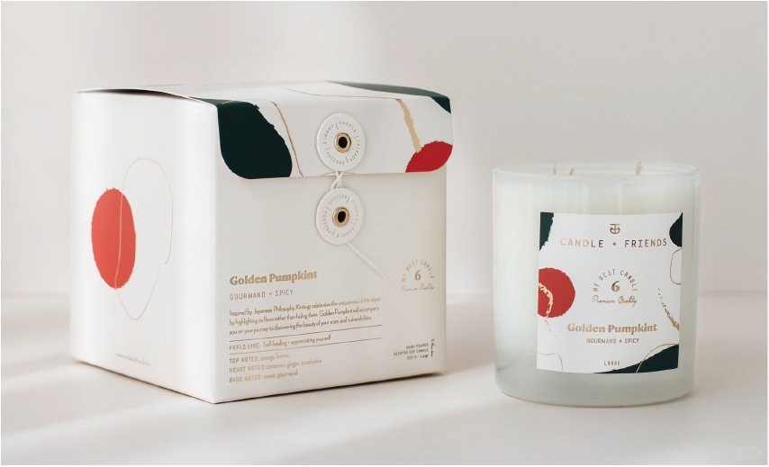 The white box has a candle next to it, the words 'Golden Pumpkin', an abstract red and green graphic on the box and a description of the scent.