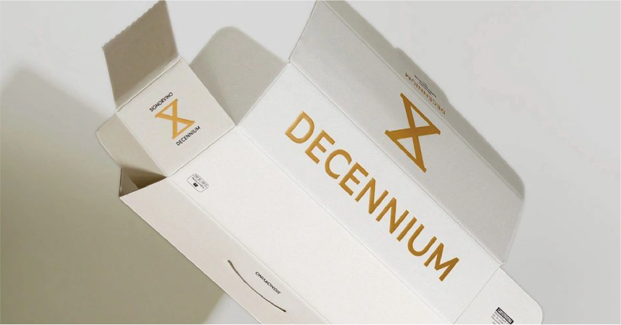 An open box on a white background with "DECENNIUM" printed in gold letters on the inside, showing the inner structure of the box.