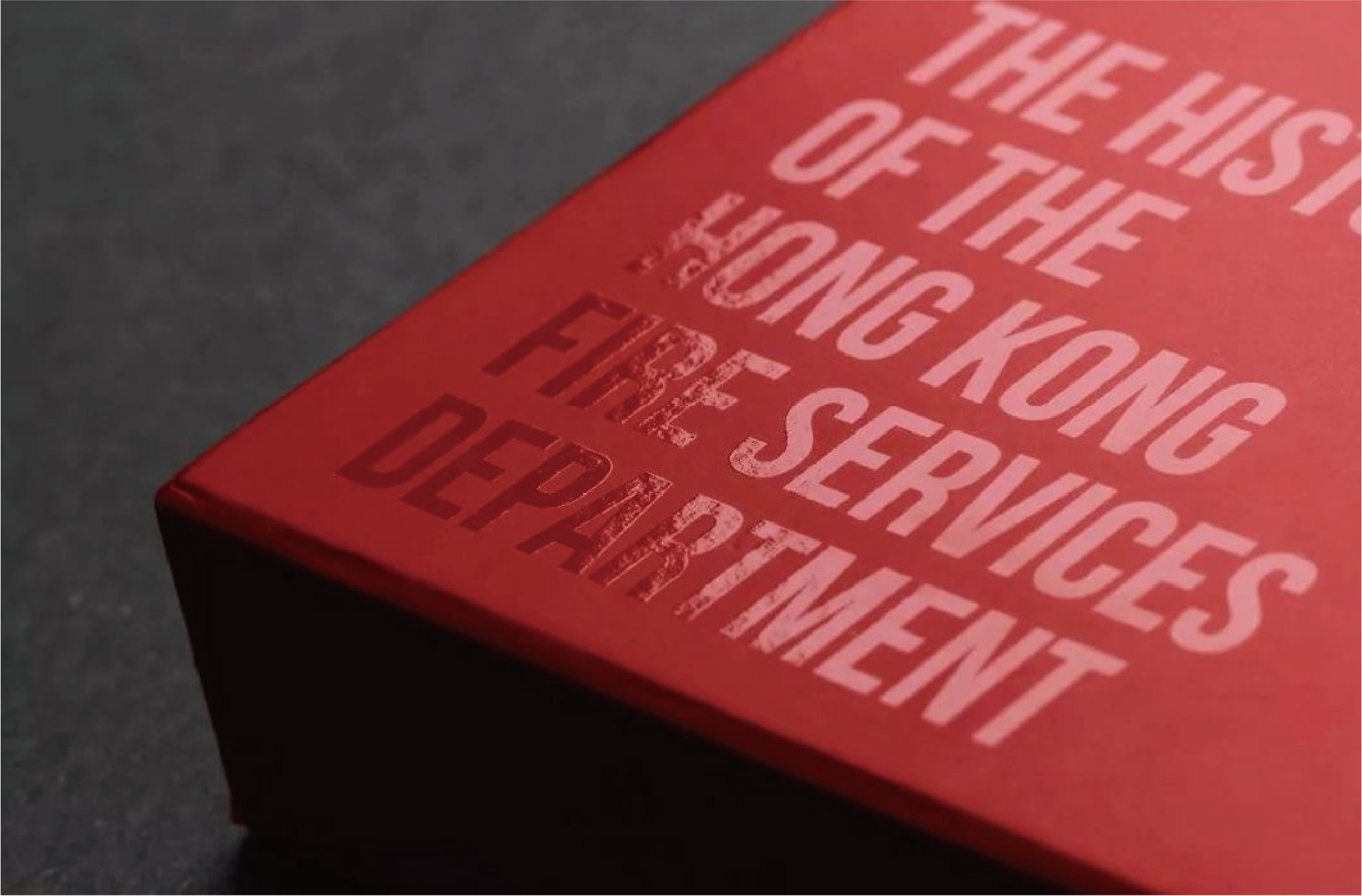 This picture shows the red cover of a book with the words "THE HISTORY OF THE HONG KONG FIRE SERVICES DEPARTMENT" printed in raised lettering, the colour of the lettering being slightly lighter than that of the cover.