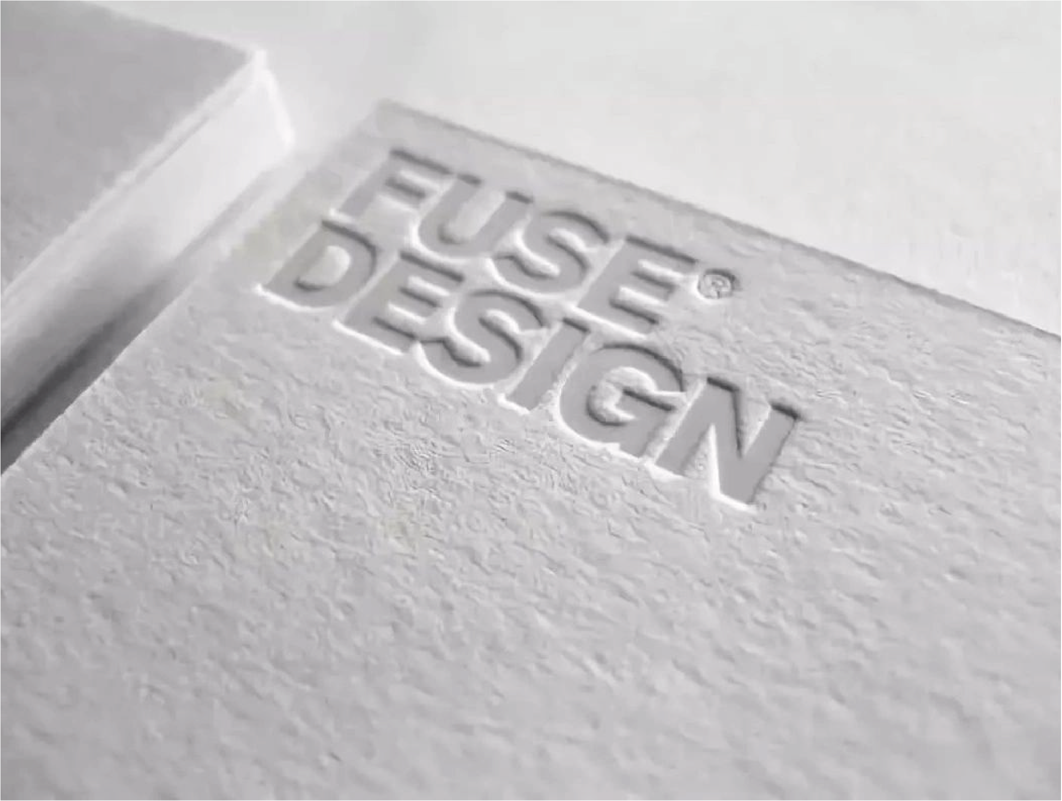 A three-dimensional effect using a concave template is used for the logo "FUSE DESIGN" recessed on a grey textured background. The trademark registration symbol® is located to the right of the word FUSE.