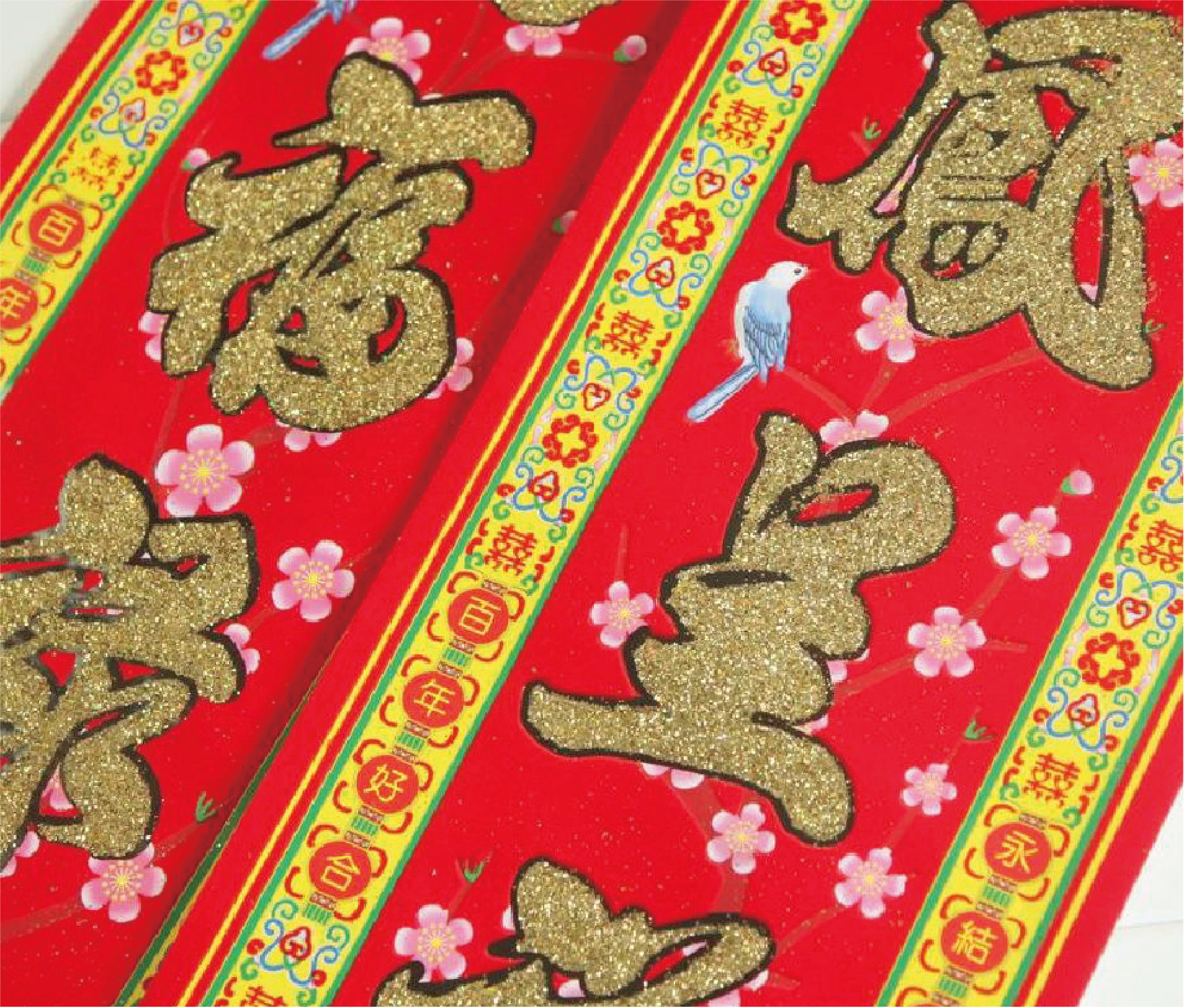 The picture shows a festive red spring scroll with the words "Good fortune and longevity" written in gold, surrounded by golden plum blossoms and a blue bird. The edges of the couplet are decorated with traditional patterns in yellow and green.