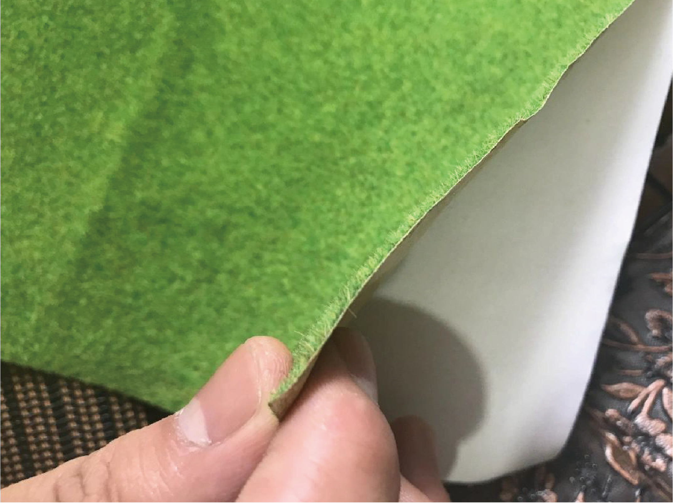 The image shows a person's fingers holding a piece of green paper or fabric, which appears to be suede or felt in texture, with a distinct thickness and texture at the edges.