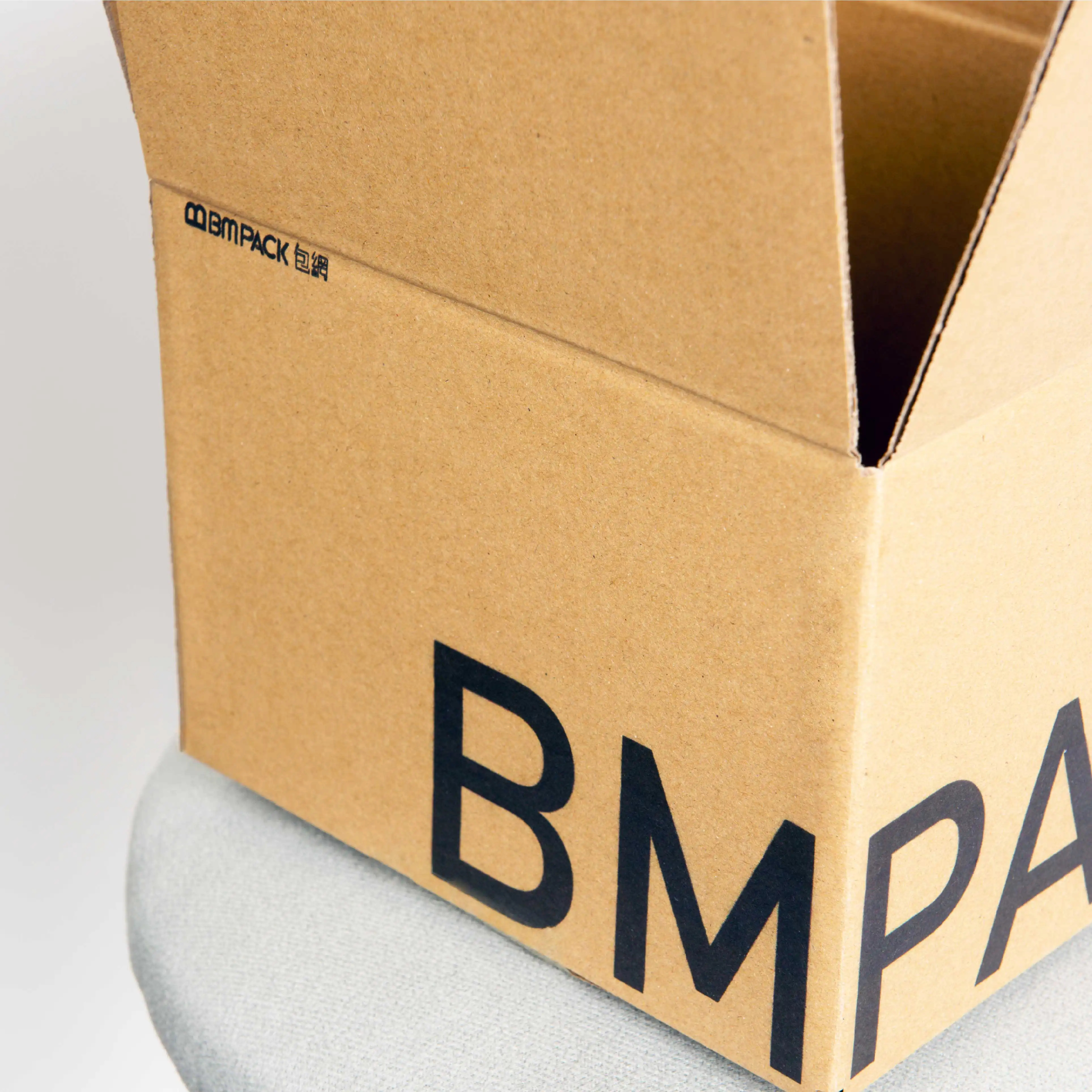 A carton box is leaning against a grey background with the large black 'BMpack' brand logo clearly displayed on the front.