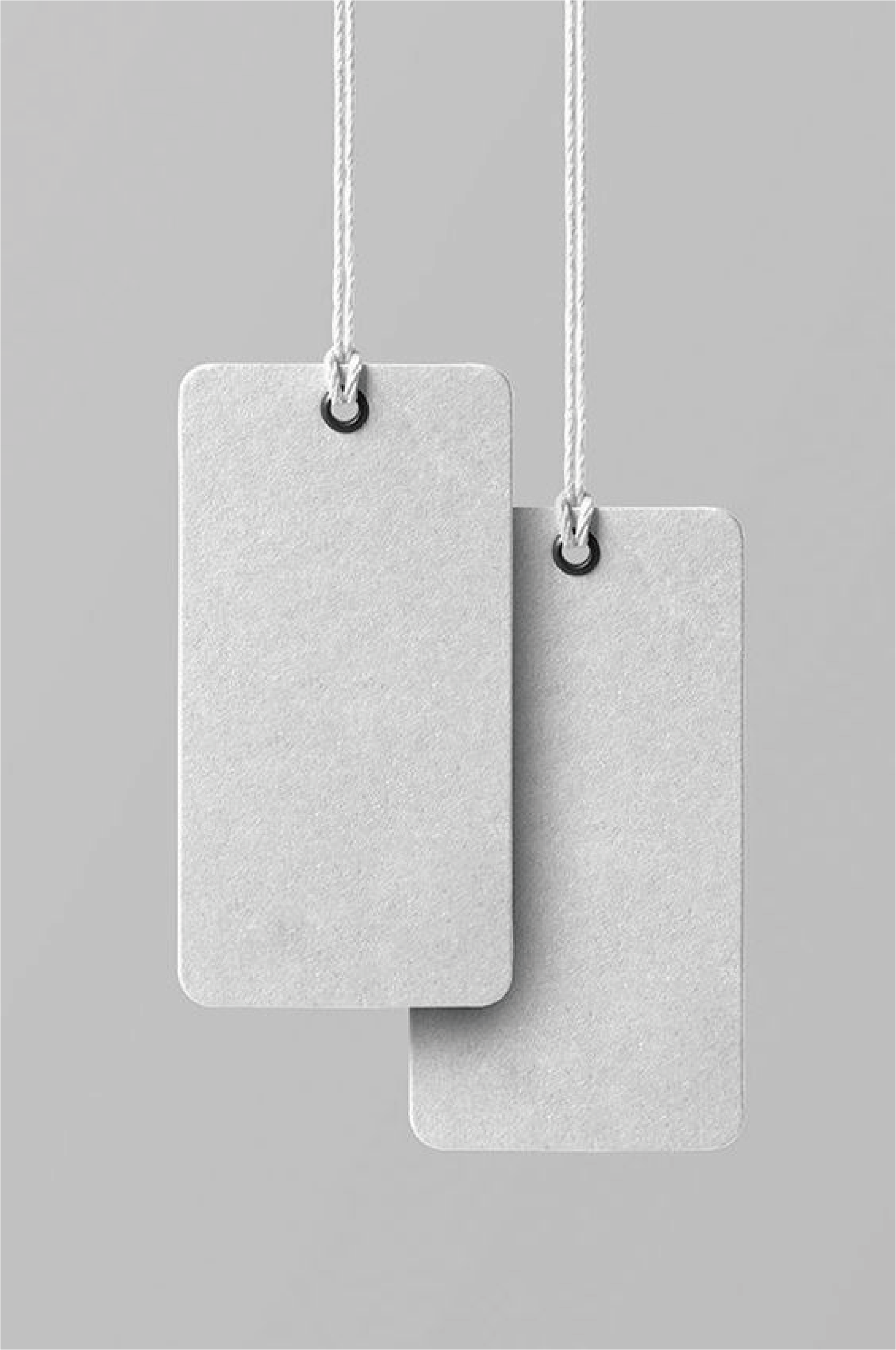 These are two hanging white kraft paper labels in front of a grey background. The labels show the irregular grain and raw texture of the kraft paper. The soft colour of white kraft paper is ideal for brands that are looking for a natural and minimalist design concept.