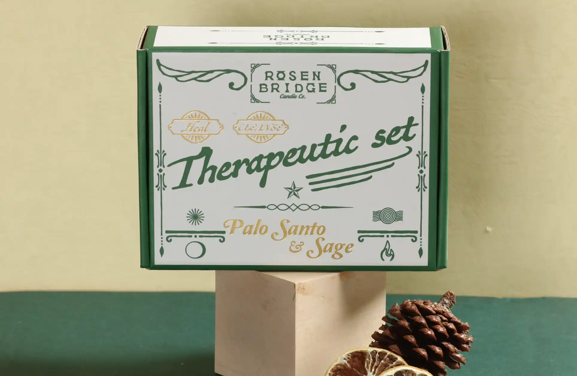 This is a green matt white card box set on a beige background. The front of the box is printed with delicate gold and white patterns, text and images in a full colour palette.